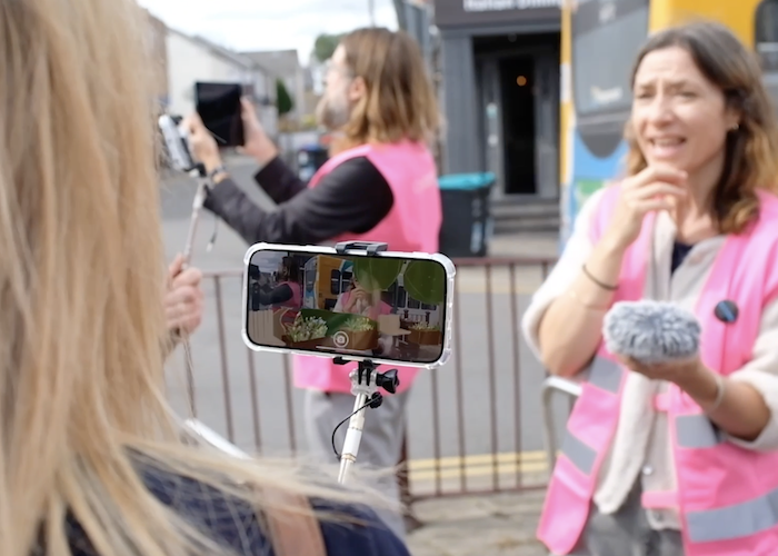 Over the shoulder view of participant looking at AR image on phone with facilitator in hi-vis talking to them